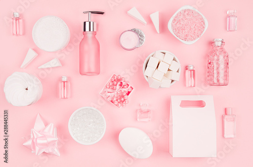 Cosmetic products and accessories in pink color - cream, bath salt, essential oil, soap, towel, sponge, pearls, bottles, bowl on pink background, top view