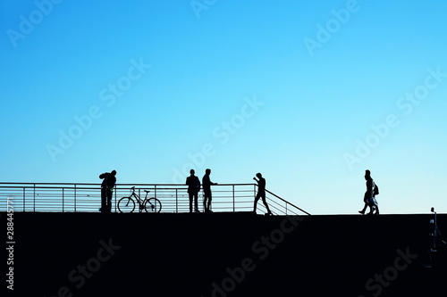 Silhouetted people relaxing and walking on street over clear blue sunny sky