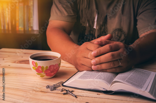 Christian man Bible study. Christian hand while praying and worship for christian religion with blurred of her body background, Casual man praying with her hands together over a closed Bible. freedom.