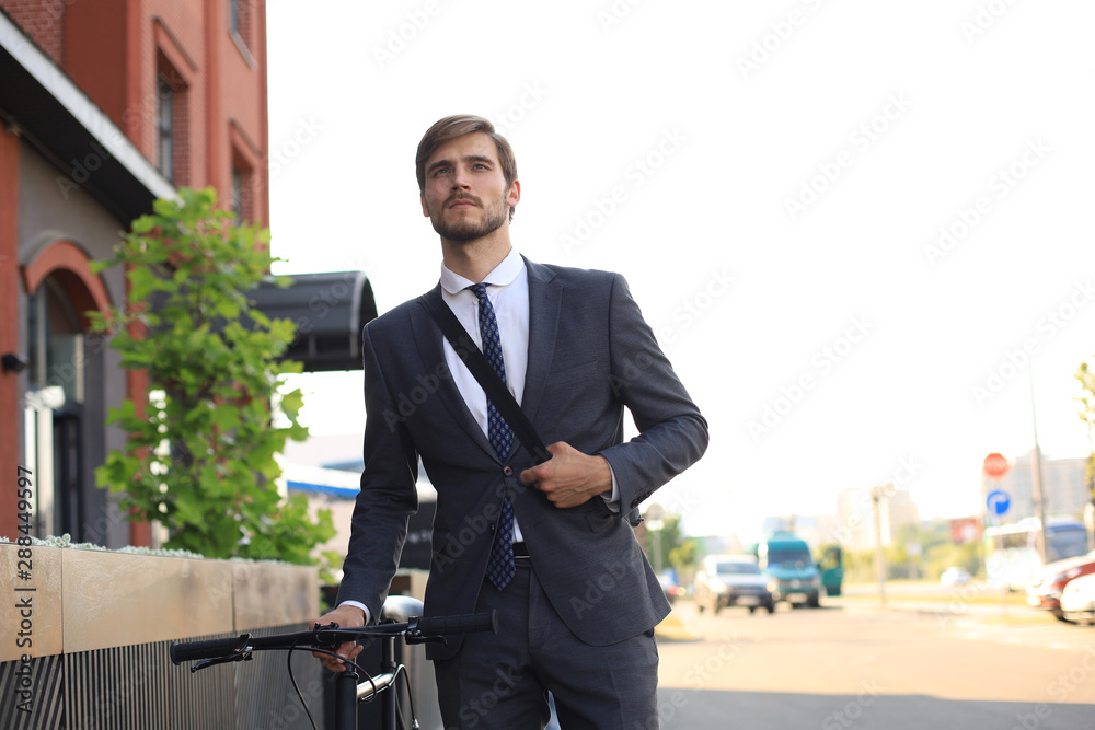 Pensive young businessman walking with bicycle on the street in city. Pensive young businessman walking with bicycle on the street in city.