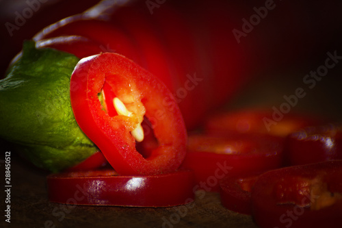 Bottom view of two chili peppers. Slices next to it. warm colors macro photo. Peppers lie on brown wood.