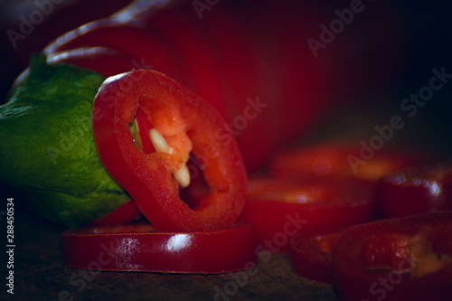 Bottom view of two chili peppers. Slices next to it. warm colors macro photo. Peppers lie on brown wood.