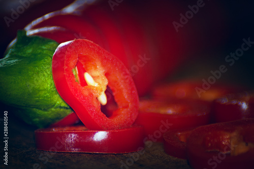 Bottom view of two chili peppers. Slices next to it. warm colors macro photo. Peppers lie on brown wood.