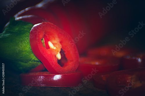 Bottom view of two chili peppers. Slices next to it. warm colors macro photo. Peppers lie on brown wood.