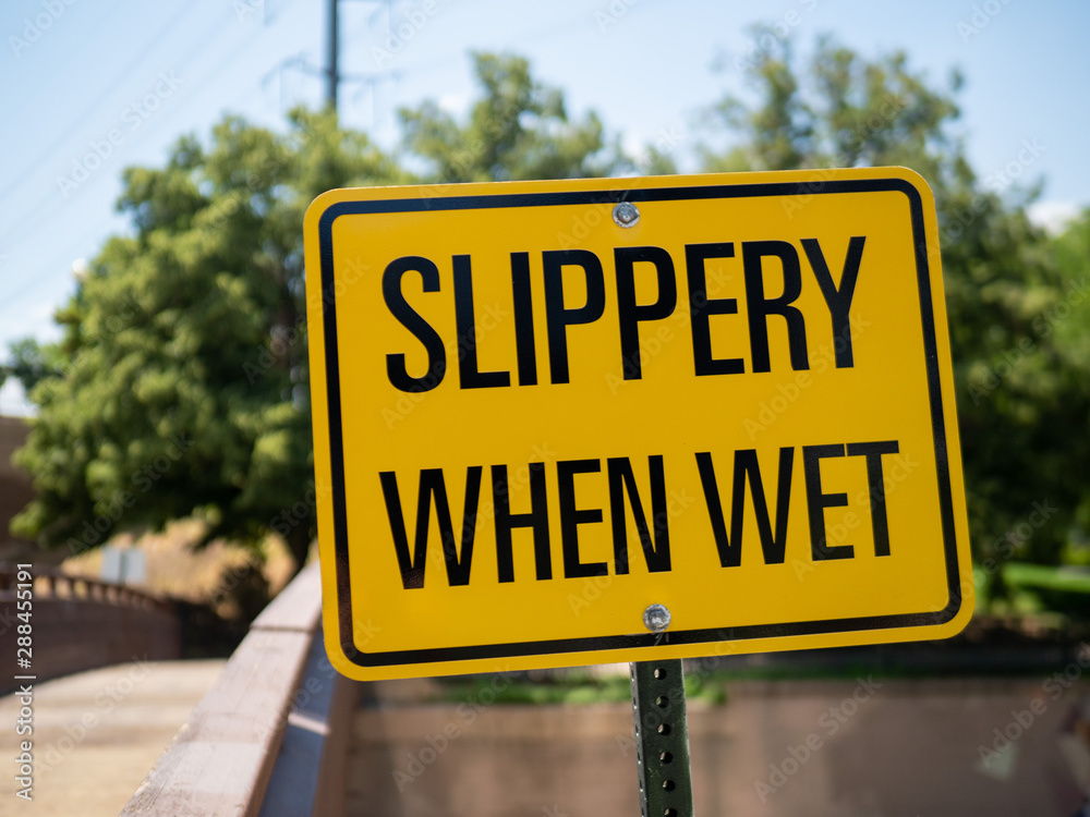 Slippery when wet yellow sign posting outdoors in front of bridge Slippery when wet yellow sign posting outdoors in front of bridge