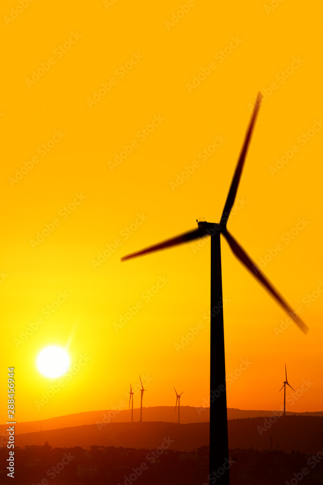 Obraz premium silhouetted windmills on hill over orange colored sunrise sky