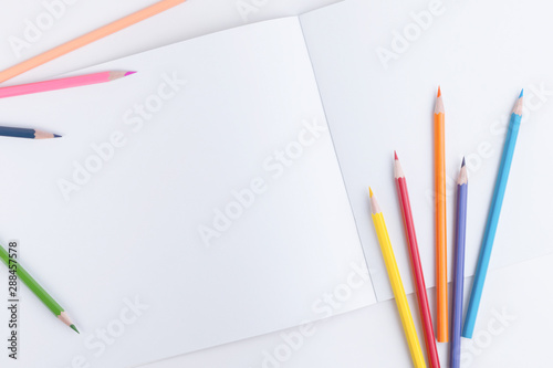 Beautiful designer composition with a group of scattered colored wooden pencils and an open sketchbook with empty pages for text, picture or other design element
