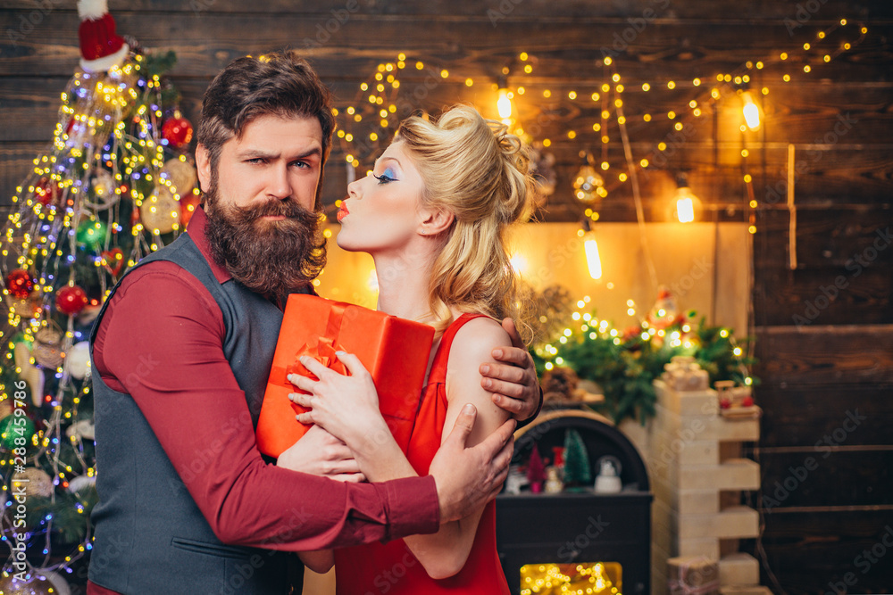 Beautiful Christmas family couple smiling with gift - wish you Happy New Year. Young Christmas fashion couple. Funny couple with colorful make-up and retro hairstyle for Christmas or New Year party. - obrazy, fototapety, plakaty 