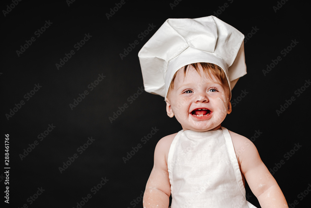 Charming toddler baby in hat of cook and apron laughing happily Charming toddler baby in hat of cook and apron laughing happily