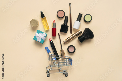 Makeup brushes and various cosmetics and a shopping cart flat lay background.