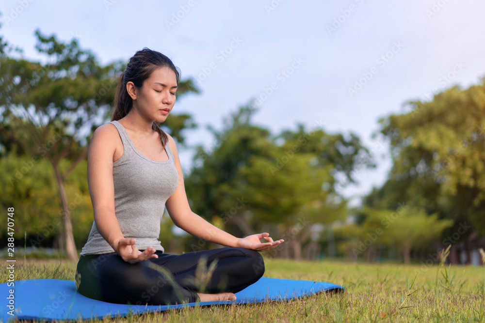 Asian woman meditating and sit in the lotus pose at park, Healthy and Yoga Concept,Mind-body improvements concept, Selective focus, Copy space.