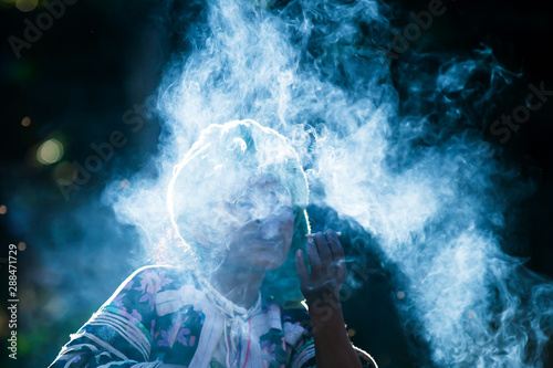 Senior Lahu woman smoking cigarette in sunrise.