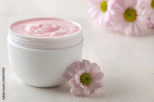 Cream. cosmetics for face and body. Pink cream and flower in a white jar on a white wooden table