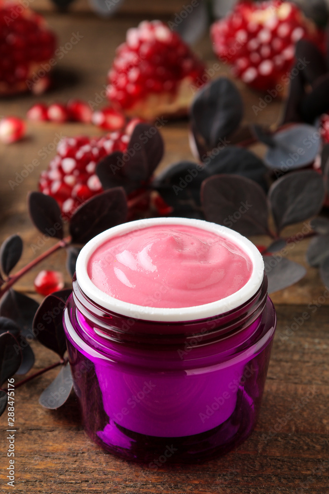 Cream. cosmetics for face and body. Pink cream and flowering branches and pomegranate in a purple jar on a brown wooden table. Cream. cosmetics for face and body. Pink cream and flowering branches and pomegranate in a purple jar on a brown wooden table.