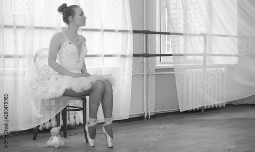 Fototapeta Naklejka Na Ścianę i Meble -  Young ballet dancer on a warm-up. The ballerina is preparing to perform in the studio. A girl in ballet clothes and shoes kneads by the handrails.