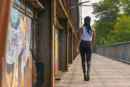 Trendy African woman walking away across a bridge