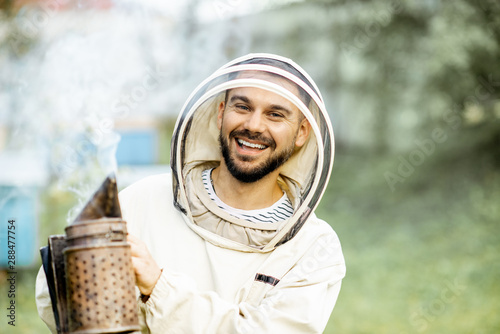 Foto Portrait of a cheerful beekeeper in protective uniform with bee smoker on the ap