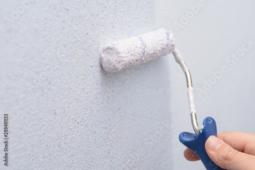 male hand with a roller for painting walls. The painter applies decorative paint to the wall. Concept - repair inside the house