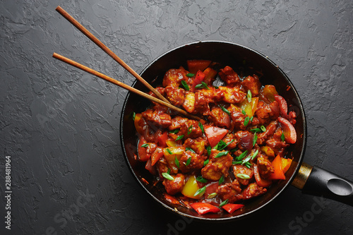 Chicken Manchurian in pan at black concrete background. Chicken Manchurian is Indian Chinese cuisine dish with Chicken breasts, bell pepper, tomatoes, soy sauce. Copy space