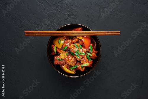Chicken Manchurian in bowl at black concrete background. Chicken Manchurian is Indian Chinese cuisine dish with Chicken breasts, bell pepper, tomatoes, soy sauce. Copy space