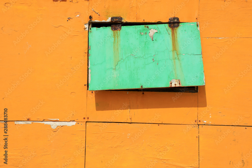 Naklejka premium Close up old peeled yellow and green colored wooden wall and window detail of building exterior