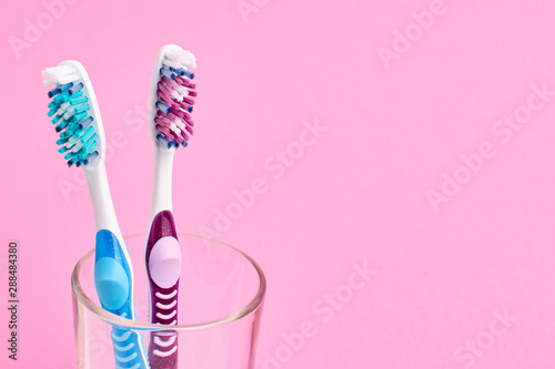 Two different colorful toothbrushes in a glass. Oral hygiene concept. Pink background. Copy space in the right.