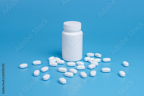 White pills, tablets and white bottle on blue background