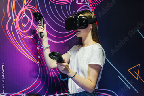 Woman playing game using virtual reality headset and gamepads in the dark room of the playing club photo