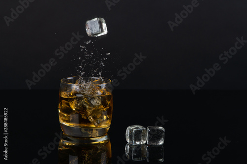Glass of whiskey with splash, on a black background. old barrel. ice