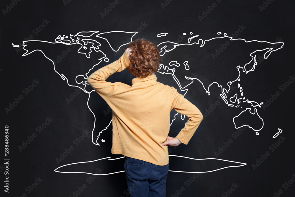 Child boy student looking at map of Earth on chalkboard background and learning geography