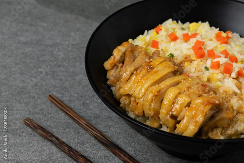 Fried rice with roast chicken and carrot in Korean style in black bowl on table.