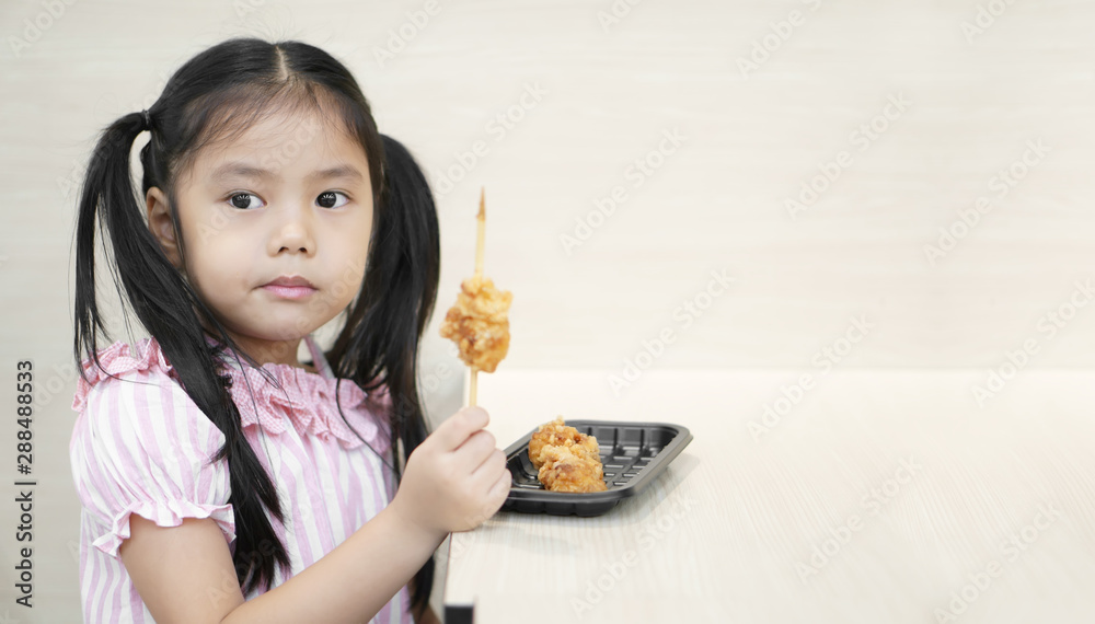 Asian child hungry or kid girl enjoy eating fried chicken food or meat ball skewers but careful of dangers of sharp wood for delicious and happy smile for lunch or breakfast at food court restaurant Asian child hungry or kid girl enjoy eating fried chicken food or meat ball skewers but careful of dangers of sharp wood for delicious and happy smile for lunch or breakfast at food court restaurant