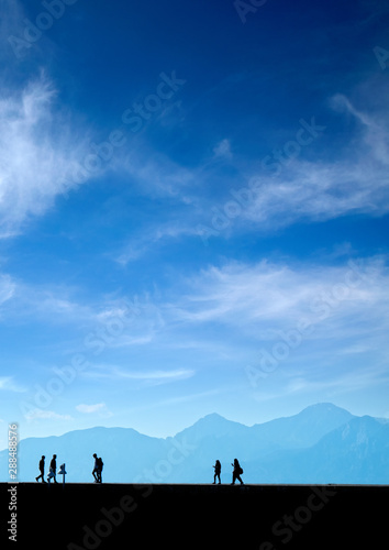 Silhouetted people walking on street over blue sky © jokerpro