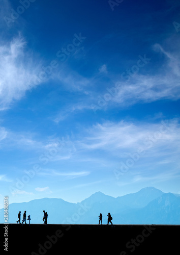 Silhouetted people walking on street over blue sky