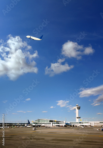 Transportation image of flying commercial passenger airplane over airport and sunny blue sky