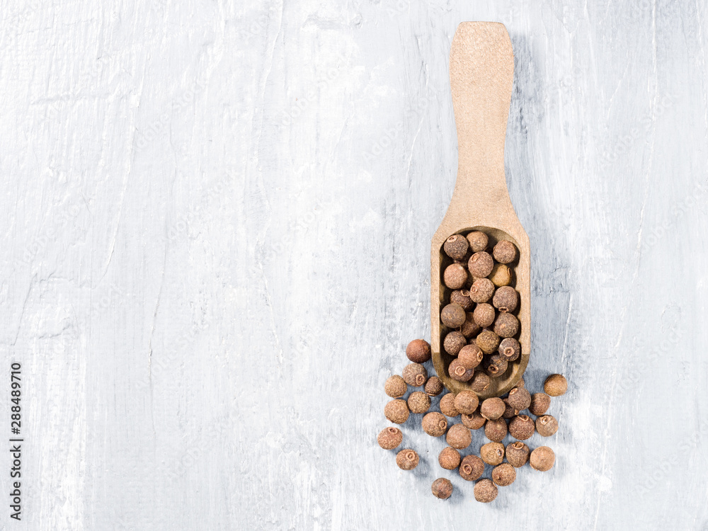 Allspice (Jamaica pepper) on a wooden scoop on a gray background vertically Allspice (Jamaica pepper) on a wooden scoop on a gray background vertically
