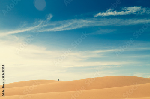 One people in the distance walk on top of a hill in the desert.