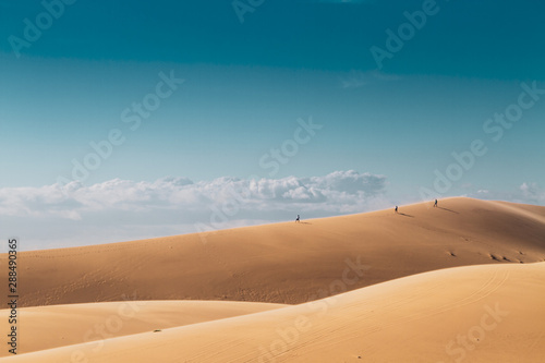 Three of people in the distance walk on top of a hill in the desert.