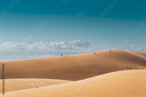 Three people in the distance walk on top of a hill in the desert.