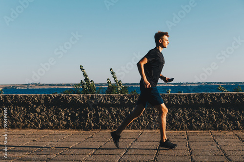 Young man is running in a park at sunrise.