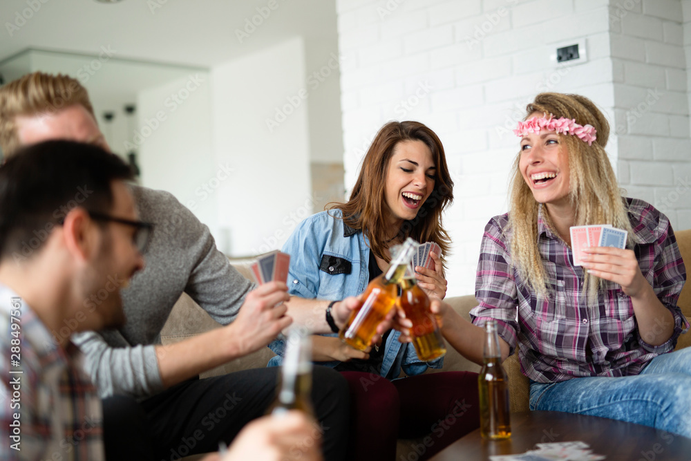 Group of happy friends playing cards and drinking