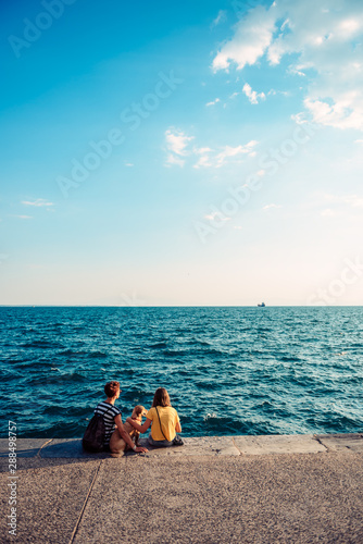 Canvas Print Mother and daughter sitting on the waterfront with dog