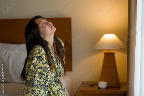 morning lifestyle portrait of young beautiful and natural Asian Japanese woman drinking coffee in bed after wake up smiling happy and cheerful enjoying the view relaxed
