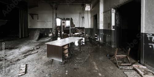 Ruined office with a destroyed desk, a turned-over chair, and a dirt-covered floor found in an abandoned, dilapidated Detroit factory, conveying a feeling of emptiness and sad desertedness