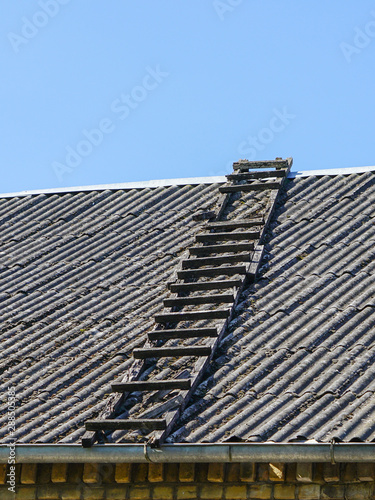 old wooden ladder on slate roof with blue sky in background © Zigmunds