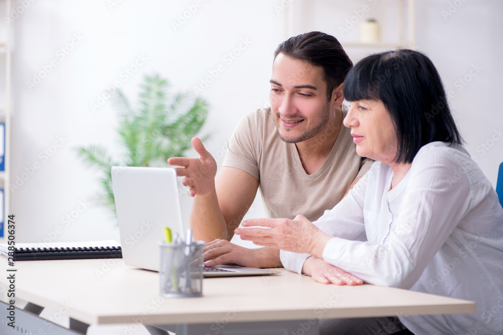 Young male employee explaining to old female colleague how to us Young male employee explaining to old female colleague how to us