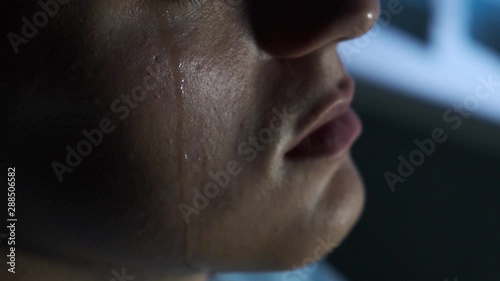 A tear flows down the cheek of a young guy, slow motion, close-up photo