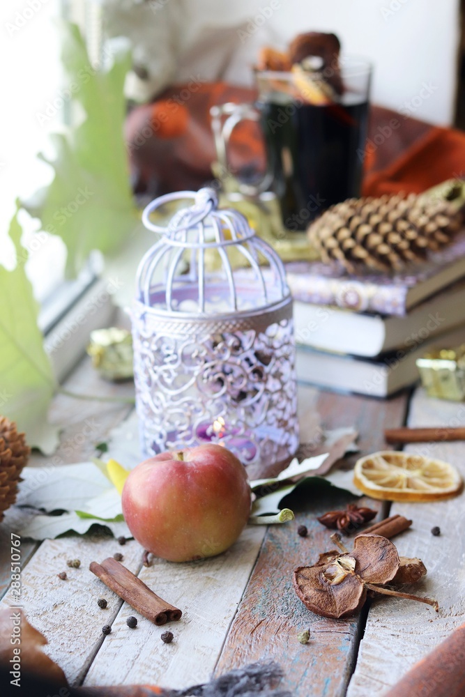 Cup with mulled wine, autumn leaves, seasonal fruits and vegetables, decor, spices on a window background, home comfort concept