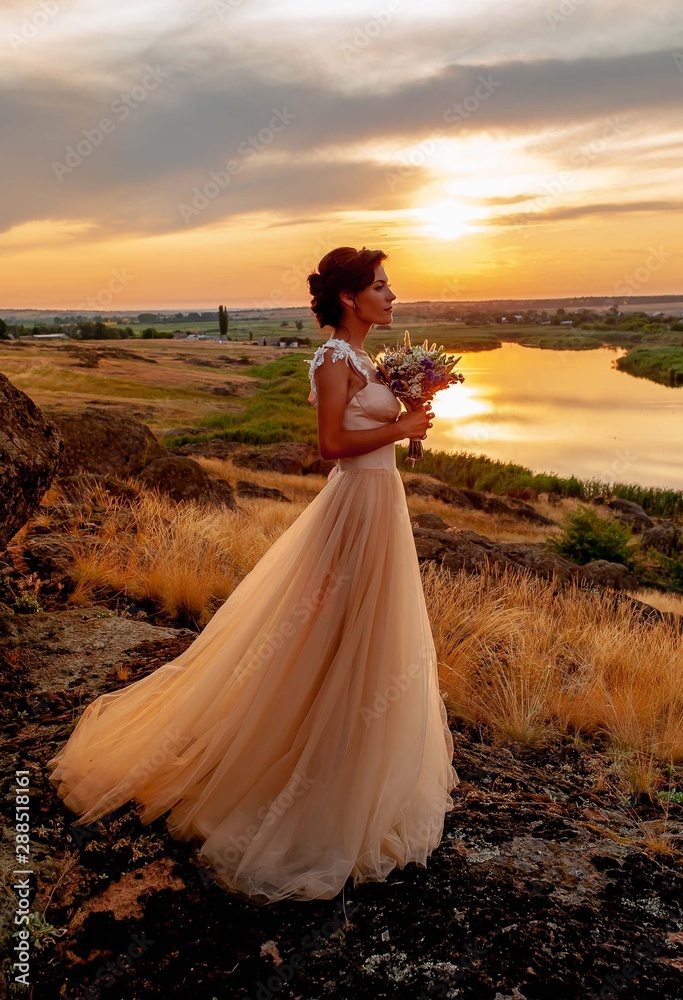 girl, the bride stands on the mountain in a dress at sunset on the background of the river, wedding day