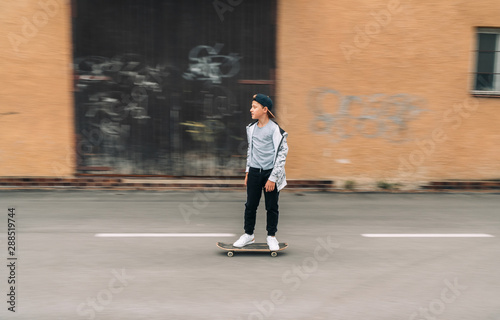 Teenager skateboarder boy riding on skateboard on asphalt road near a grunge graffiti wall. Youth generation Freetime spending concept image. © Soloviova Liudmyla